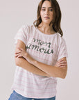 Front view of woman wearing Chaser’s white Mon Amour Stripe Tee with “mon amour” French text and light pink stripes on a plain background