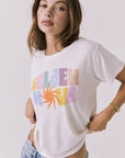 3/4 view of a woman wearing Chaser's white Golden Hour Tee with colorful graphic design on a plain background