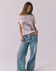 Full body front view of a woman wearing Chaser's the Grateful Dead 60 Years so Far pink tee with a graphic design and blue jeans on a plain background
