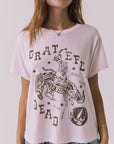 Close up view of a woman wearing Chaser's the Grateful Dead 60 Years so Far pink tee with a graphic design on a plain background