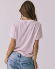 Back view of a woman wearing Chaser's the Grateful Dead 60 Years so Far pink tee on a plain background