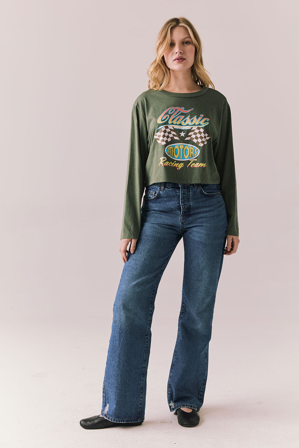 Full view of womens wearing Chaser's Classics Motors washed bronze green long sleeve with retro graphic and denim on a plain background