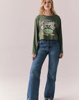 Full view of womens wearing Chaser's Classics Motors washed bronze green long sleeve with retro graphic and denim on a plain background