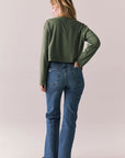 Back full view of womens wearing Chaser's Classics Motors washed bronze green long sleeve with retro graphic and denim on a plain background