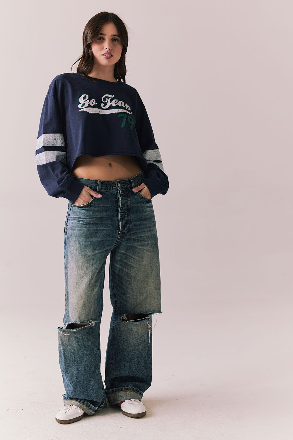 Full body view of model in Go Team long sleeve in blue with contrast cuff details and ripped jeans on a plain background