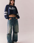 Full body view of model in Go Team long sleeve in blue with contrast cuff details and ripped jeans on a plain background