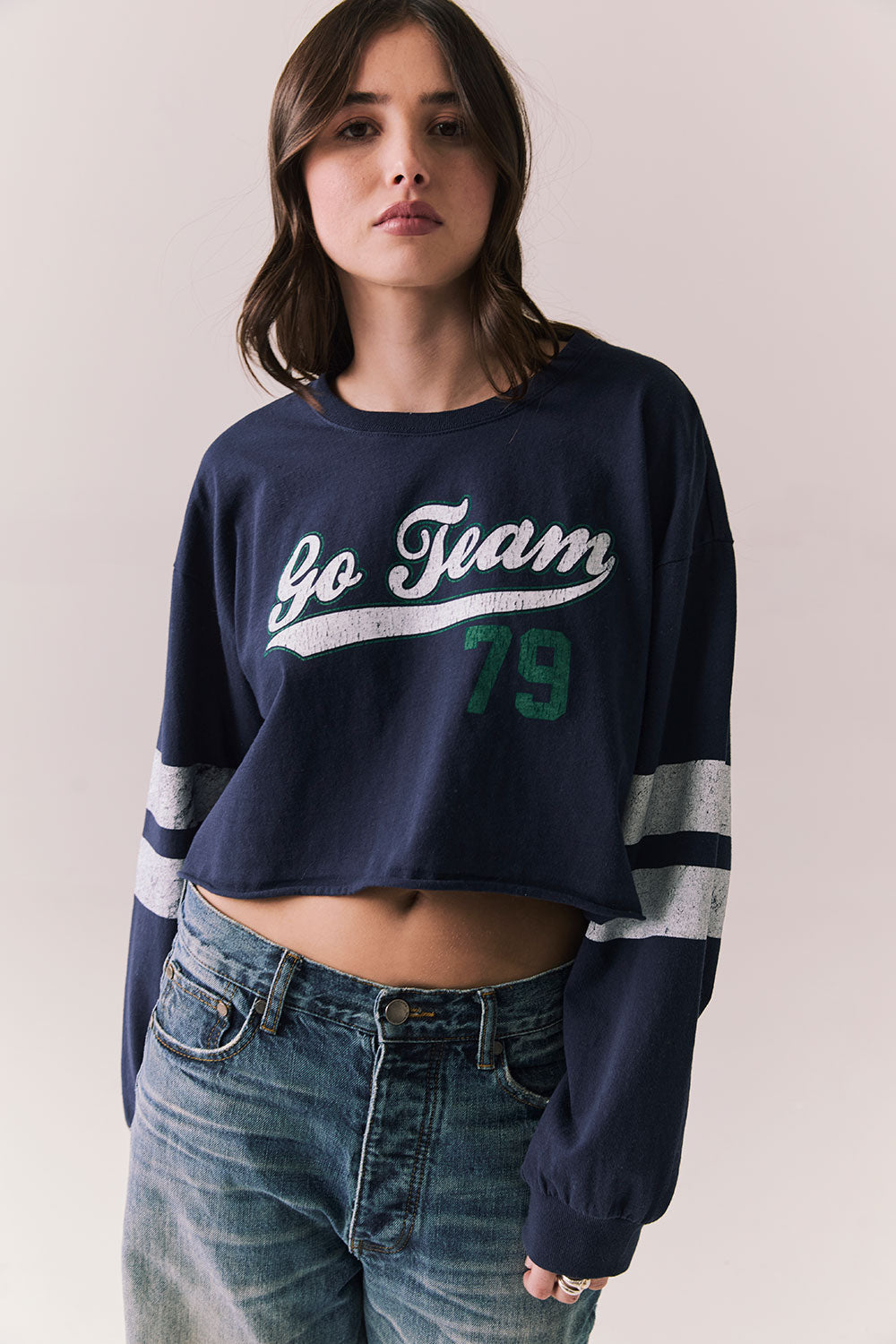 Front view of model in Go Team long sleeve in blue with contrast cuff details and jeans on a plain background
