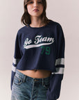 Front view of model in Go Team long sleeve in blue with contrast cuff details and jeans on a plain background