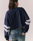 Back body view of model in Go Team long sleeve in blue with contrast cuff details and jeans on a plain background