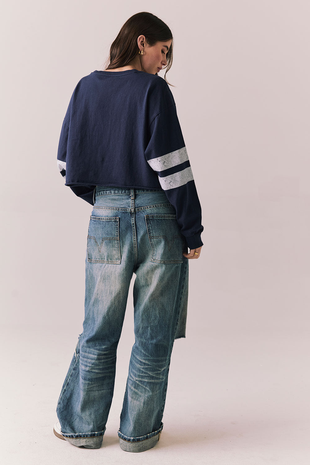 Back body view of model in Go Team long sleeve in blue with contrast cuff details and ripped jeans on a plain background