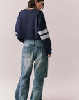 Back body view of model in Go Team long sleeve in blue with contrast cuff details and ripped jeans on a plain background