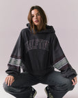 Full body view of model wearing the Halftime fleece pullover hoodie in True Black with ‘HALFTIME’ chest graphic, crouching on the floor against a plain background.