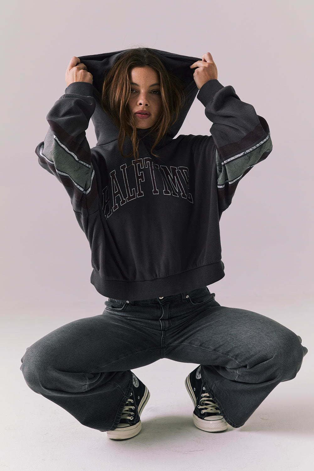 Full body view of model wearing the Halftime fleece pullover hoodie in True Black with ‘HALFTIME’ chest graphic, crouching on the floor against a plain background.