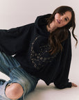 Front view of model wearing the The Grateful Dead We Are Everywhere Hoodie in True Black with cropped boxy fit and skull graphic made from stars and zodiac signs with denim sitting against a plain background