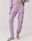 Woman wearing Chaser’s Bolt Amethyst Purple Joggers with matching pullover on a plain background