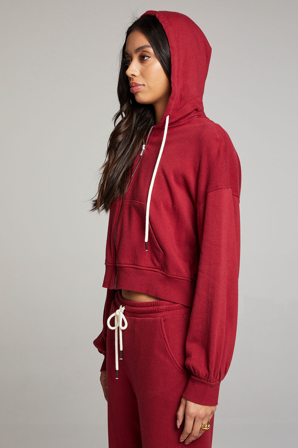 Side view of model wearing Abilenee Blood Red Zip Up Hoodie with cropped hem and hoodie up and full-zip closure against a plain background