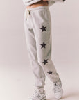 Side view of NYC Stars Joggers in Heather Grey with black star print down each leg, styled for a casual lounge look, against a plain background