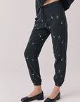 Side view of woman wearing Chaser’s black Champagne Party Joggers with allover champagne bottle and glass graphics on a light grey background
