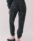 Back view of woman wearing Chaser’s black Champagne Party Joggers with allover champagne bottle and glass graphics on a light grey background