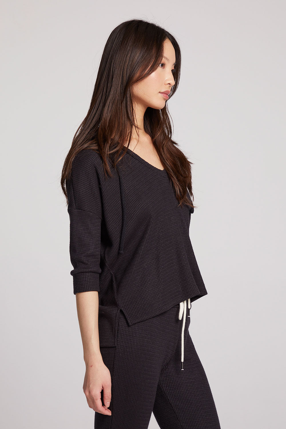 Side view of model wearing 3/4 Sleeve Split Side Licorice Dolman Hoodie in black showing relaxed fit and split-side detail on plain background
