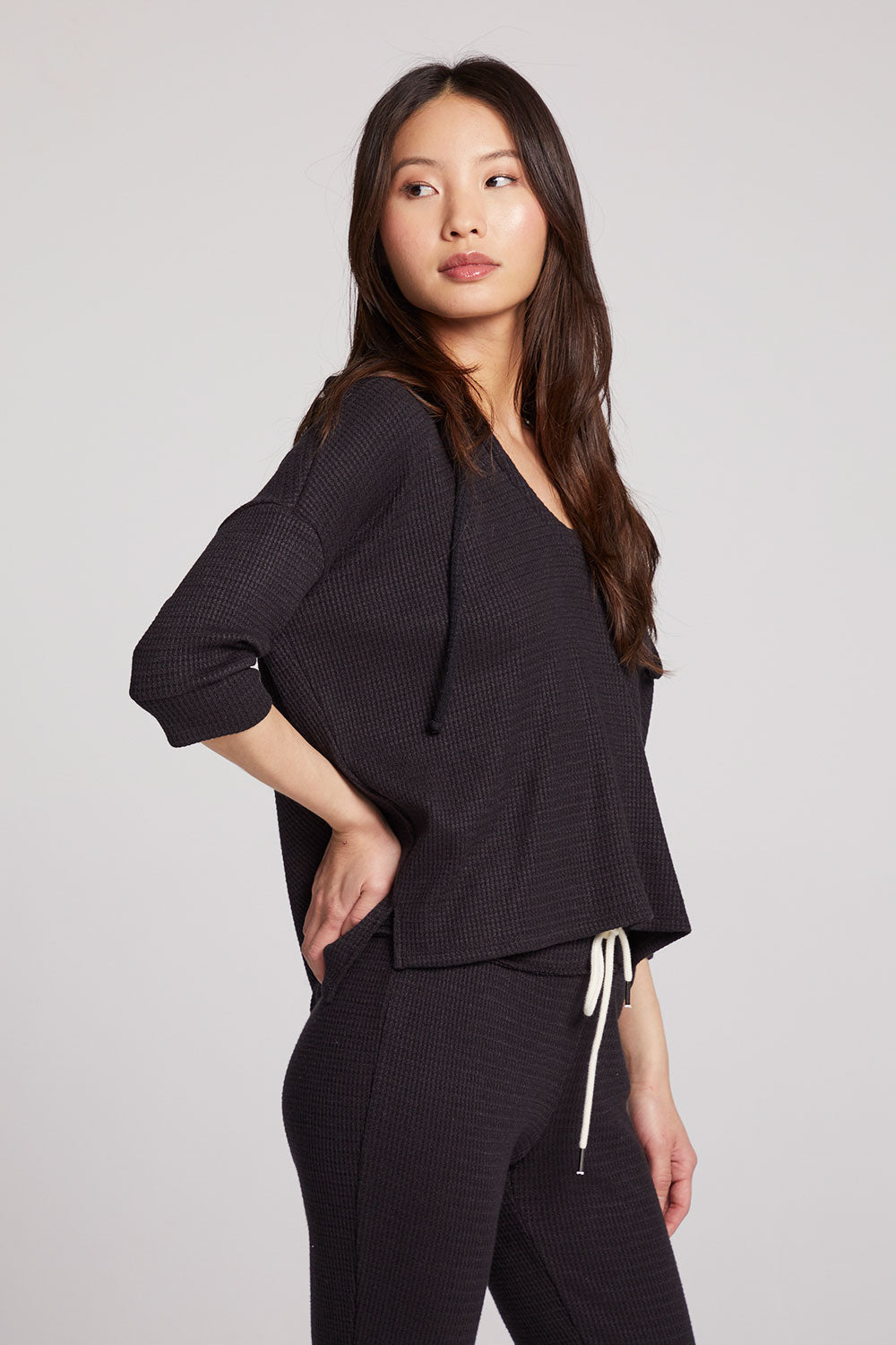 Side view of model wearing 3/4 Sleeve Split Side Licorice Dolman Hoodie in black showing relaxed fit and split-side detail on plain background