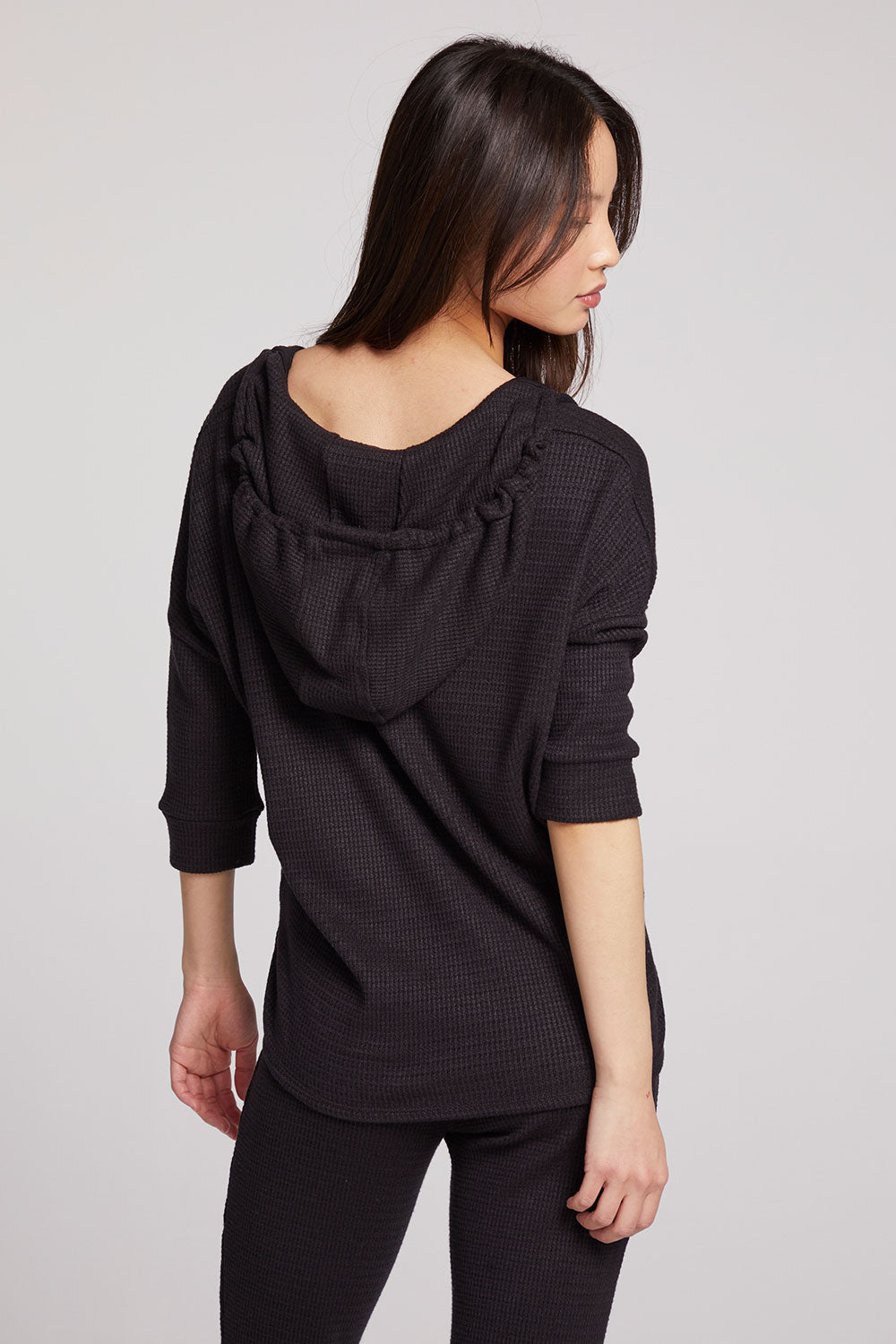 Back view of model wearing 3/4 Sleeve Split Side Licorice Dolman Hoodie in black with dolman sleeves and split-side hem on plain background