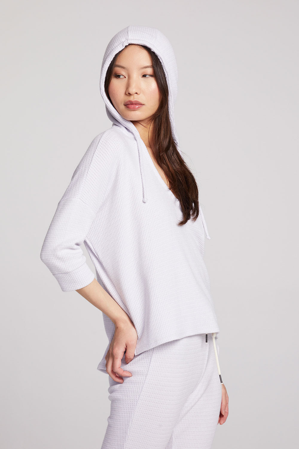 Side view of model wearing 3/4 Sleeve Split Side Light Heather Grey Dolman Hoodie with dolman sleeves and split-side hem with hoodie up on plain background with matching joggers