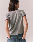 Back view of woman wearing a gray 'Coca-Cola University' t-shirt against a plain background