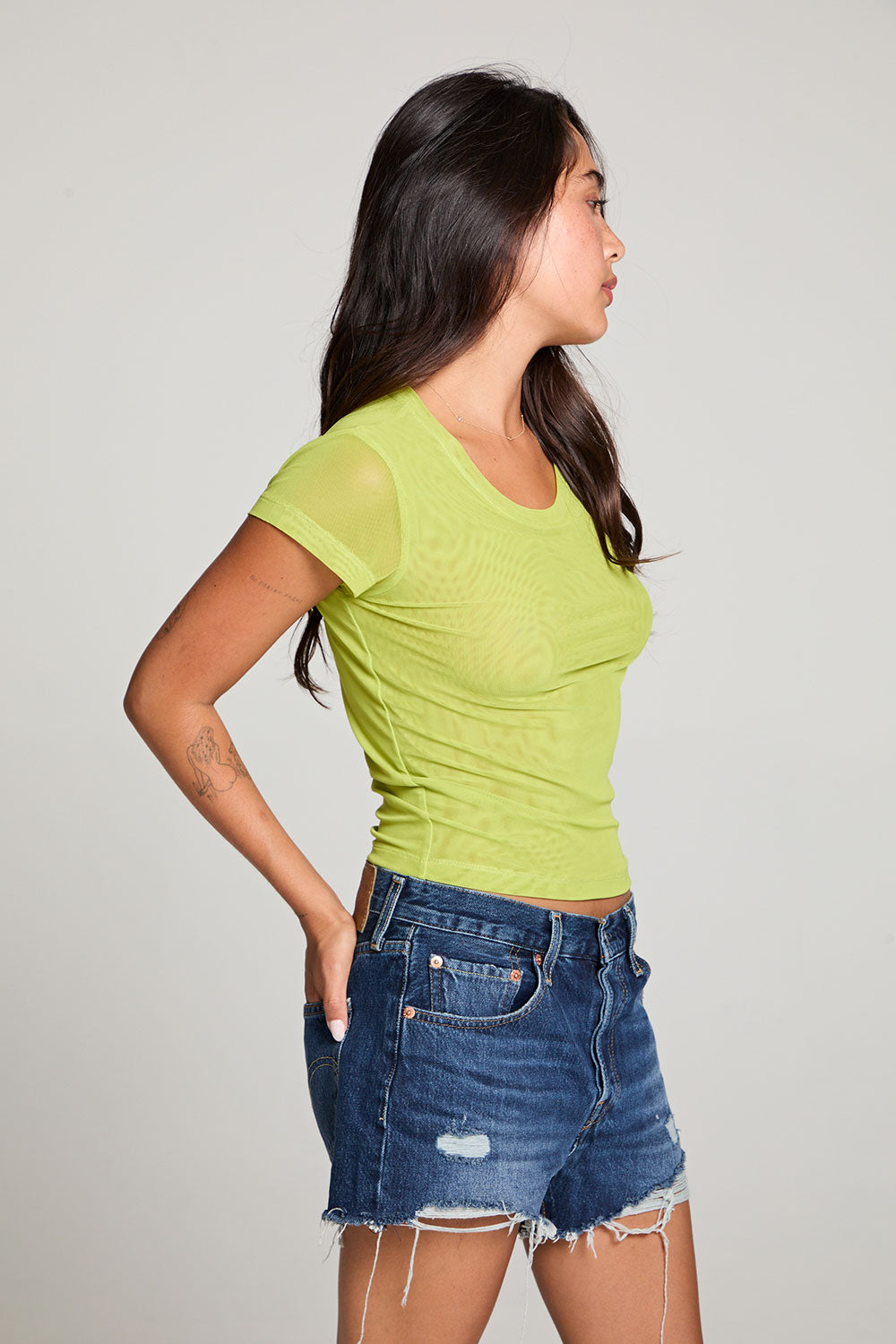Side view of model wearing the 90’s Chartreuse Baby Tee in bright green with scoop neck and fitted cropped cut and cut off denim against a plain background