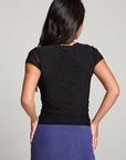 Back view of model wearing 90’s Licorice Black Baby Tee with scoop neckline and fitted waist with a purple skirt against a plain background
