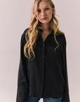 Front view of a model wearing the Helenaa button-down shirt in True Black with collared neckline and oversized silhouette, styled with relaxed jeans against a plain backdrop.