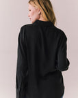 Back view of a model wearing the Helenaa button-down shirt in True Black with collared neckline and oversized silhouette, styled with relaxed jeans against a plain backdrop.