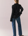 Back front view of a model wearing the Helenaa button-down shirt in True Black with collared neckline and oversized silhouette, styled with relaxed jeans against a plain backdrop.