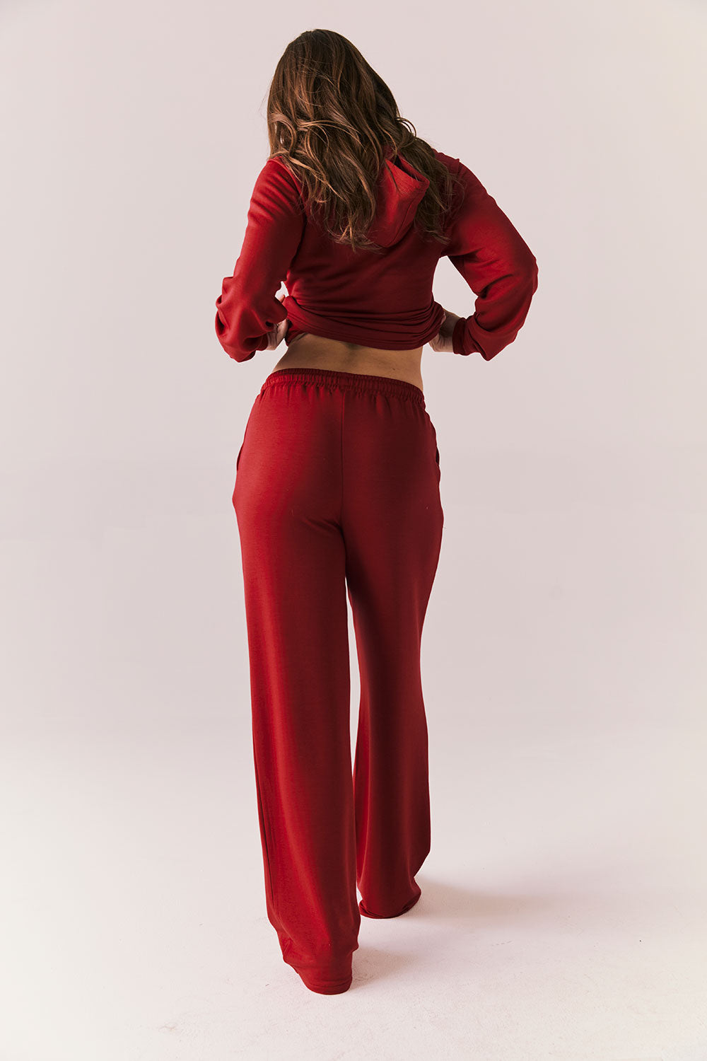 Full body back look of model wearing Sandyy Crimson Red Trousers with coordinating hoodie.