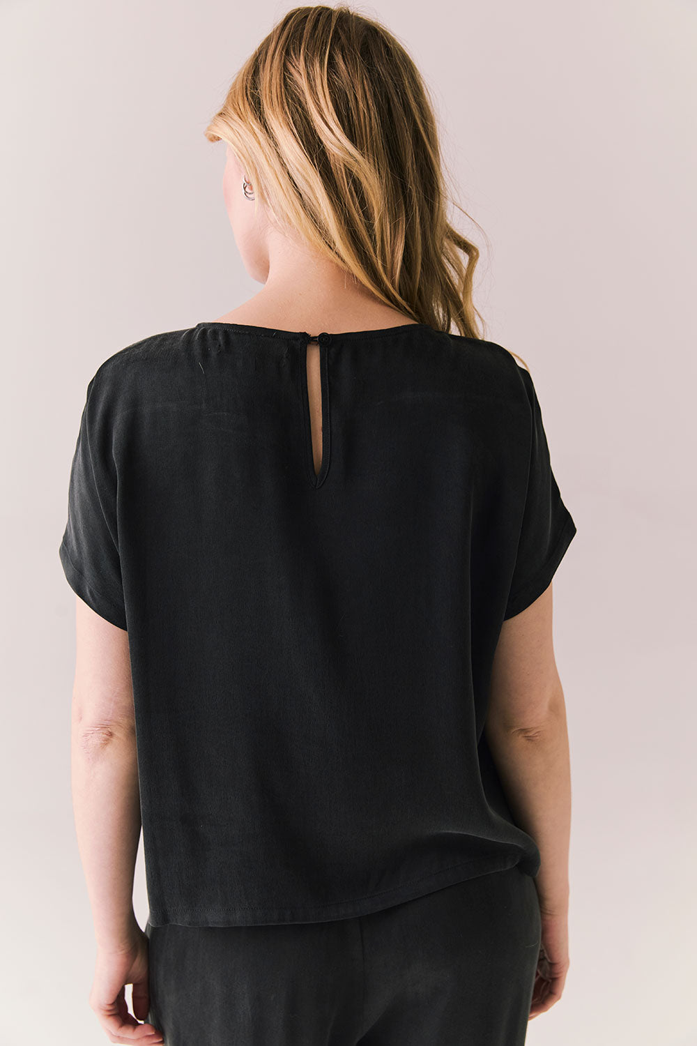 Back view of woman wearing Davis tee in true black and matching Lee Pant against a plain background