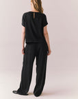 Full back view of woman wearing Davis tee in true black and matching Lee Pant against a plain background