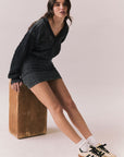 Side body view of model leaning on an apple box wearing Channel Mini Dress in silky true black