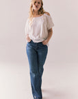 Full front view of Northridge Tee in white with cold shoulder cutout and flowy fit and blue jeans against a plain background