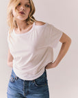 Front view of Northridge Tee in white with cold shoulder cutout and flowy fit and blue jeans against a plain background