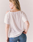 Back view of Northridge Tee in white with cold shoulder cutout and flowy fit and blue jeans against a plain background