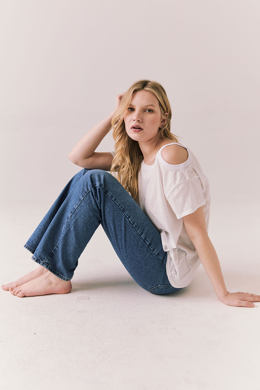Full side view of Northridge Tee in white with cold shoulder cutout and flowy fit and blue jeans against a plain background