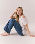 Full side view of Northridge Tee in white with cold shoulder cutout and flowy fit and blue jeans against a plain background
