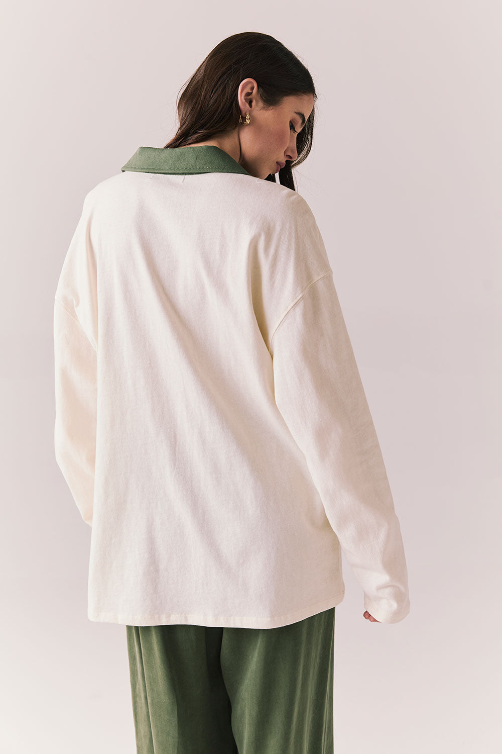 Back view of a woman wearing the color-blocked Chico Long Sleeve White and Green Rib Pullover and green pants on a white background
