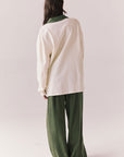 Full back view of woman wearing the color-blocked Chico Long Sleeve White and Green Rib Pullover and green pants on a white background