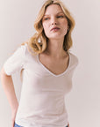 Front view of model wearing Fresno tee in white with scoop neckline and fitted silhouette and blue jeans against a plain background