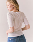 Back view of model wearing Fresno tee in white with scoop neckline and fitted silhouette and blue jeans against a plain background