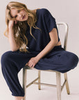 Full body view of model sitting on a chair in Billyy Joggers in midnight blue