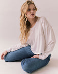 Woman sitting on the floor wearing the Hartt long sleeve in white with cotton texture and clean silhouette and blue jeans against a plain background