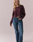 Full body view of model wearing the Hartt long sleeve tee in fig (deep purple) with clean silhouette and blue jeans, against a plain background.