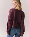 Back view of model wearing the Hartt long sleeve tee in fig (deep purple) with clean silhouette and blue jeans, against a plain background.